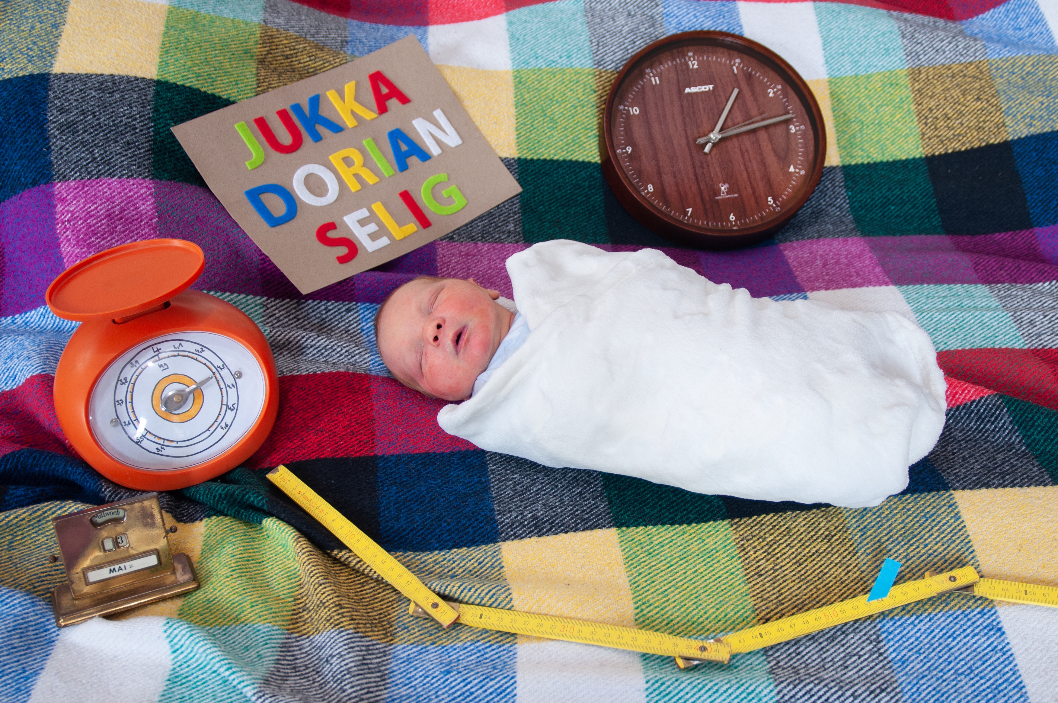 Neugeborenes Baby liegt auf dem Boden, umgeben von Gegenständen, die Auskunt über Name, Geburtsgewicht und Geburtszeit geben.